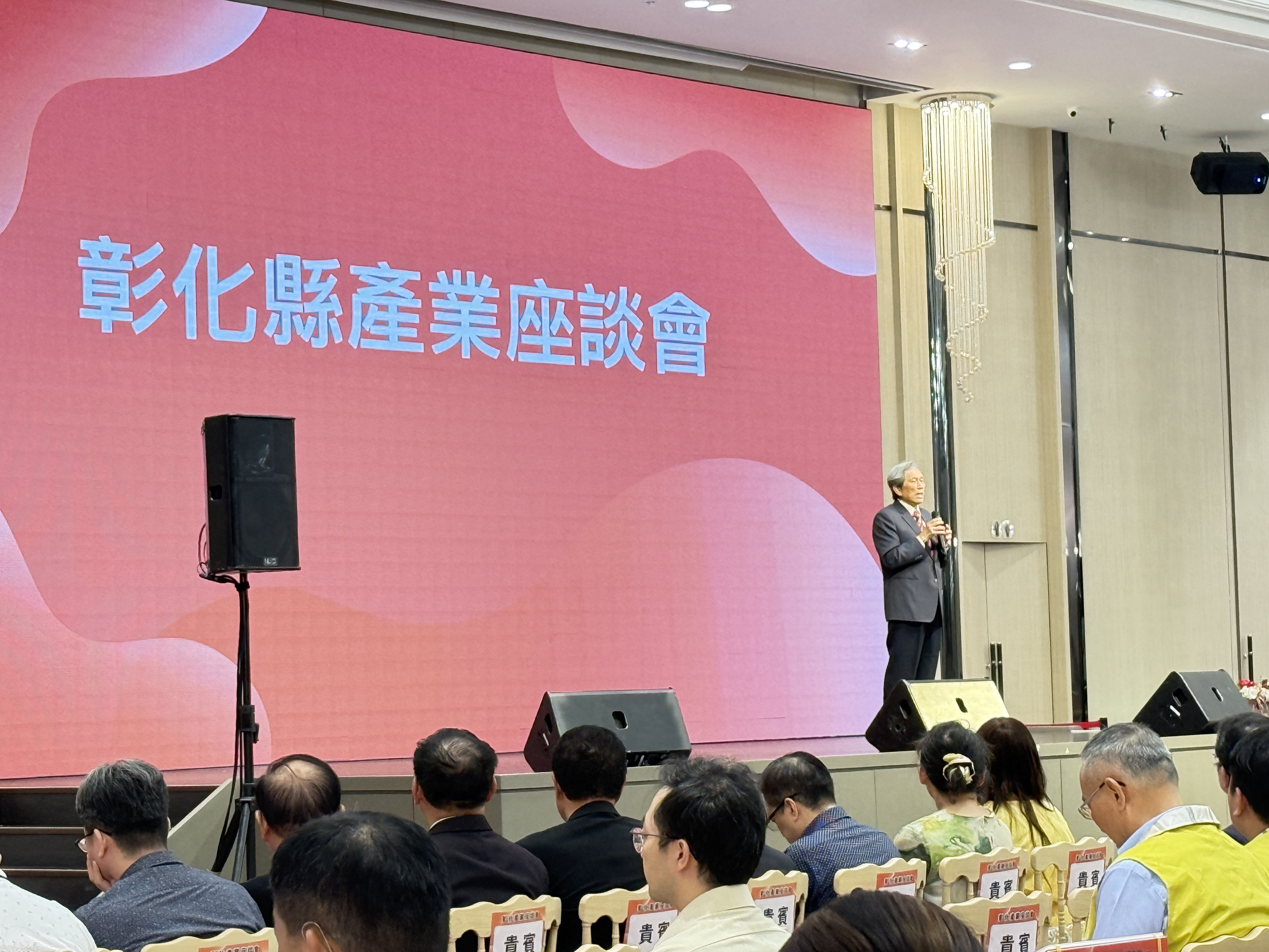 彰化縣傳統產業經濟座談會現場，講者於舞台發言，背景螢幕顯示「智慧產業新樞紐」字樣，展現產業升級主題。