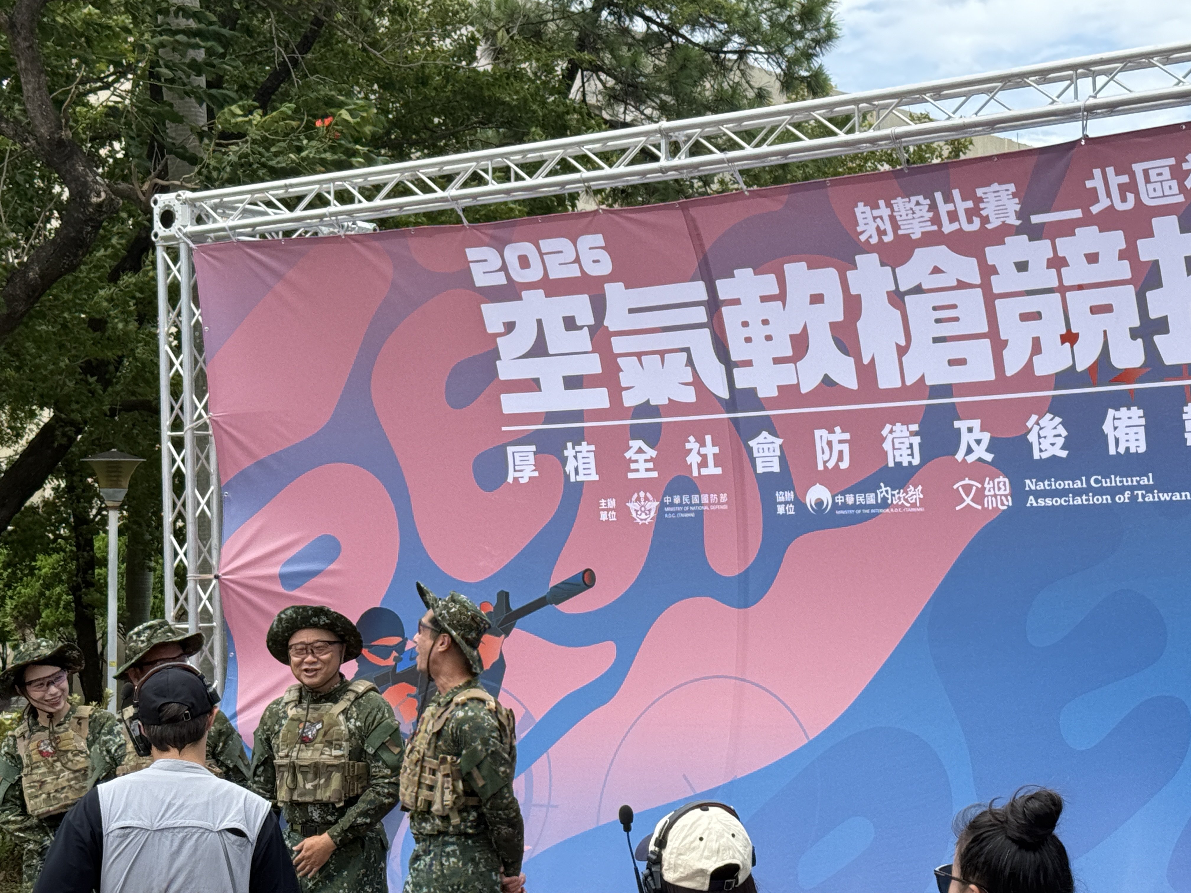 在戶外或學術場地，有學生和教官參與一項與國防相關的實作或講座活動，展現學習氣氛。
